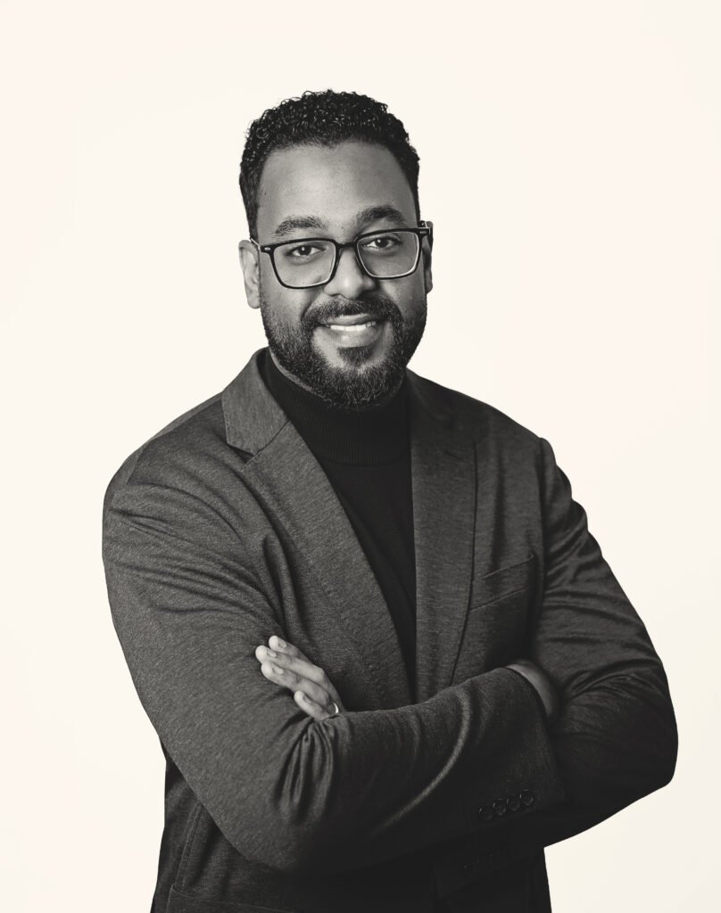 Black-and-white studio portrait of a man in a blazer with arms crossed.